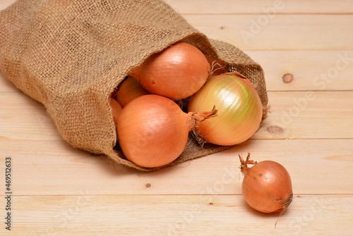 onions spilling out of burlap sack on wooden background photo