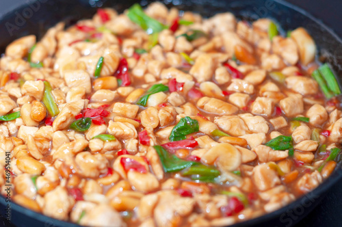 Kung pao chicken in a frying pan on a black wooden table close-up. A traditional, popular dish of Chinese cuisine consisting of chicken, peanuts, hot chili pepper, sauces and spices. photo