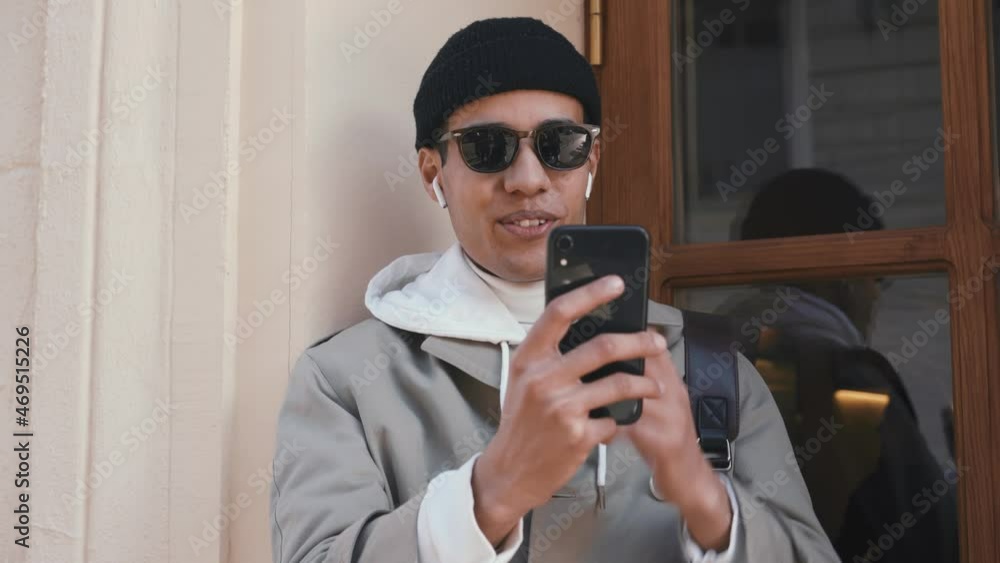 Smiling Arabian man in eyeglasses talking by phone in headphones outdoors Smiling Arabian man in eyeglasses talking by phone in headphones outdoors