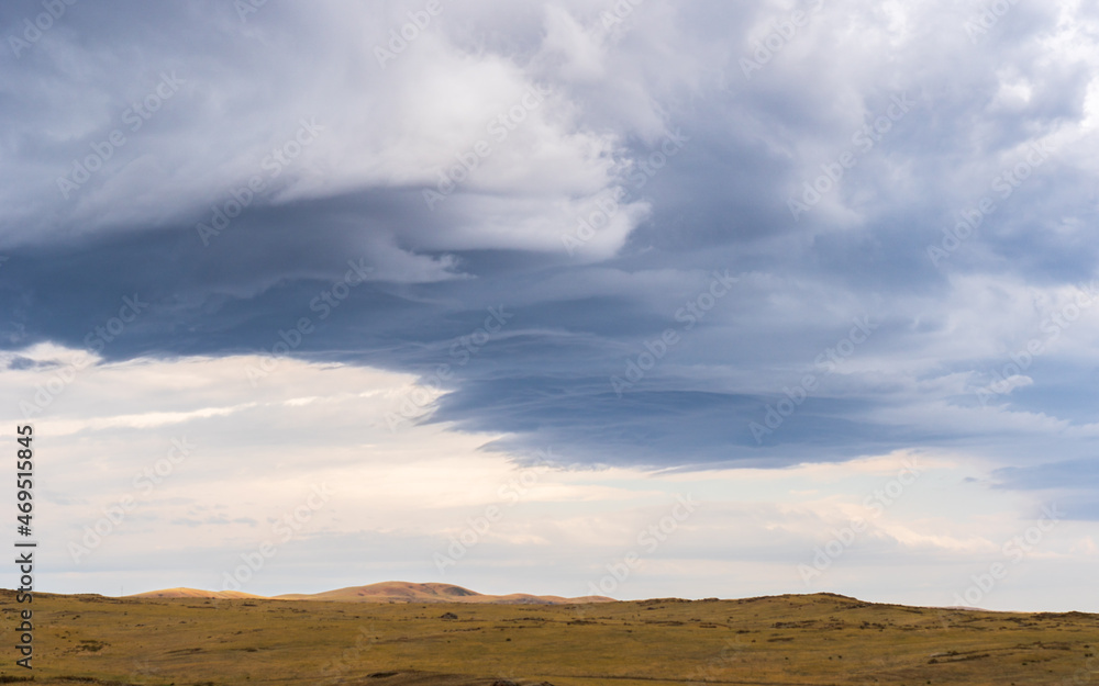 Fototapeta premium Dramatic clouds hover over the golden plains of eastern Kazakhstan, adding depth to the serene steppe landscape