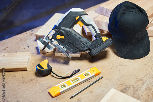 work tools and black cap on the desktop. tape measure, jigsaw with battery, building level