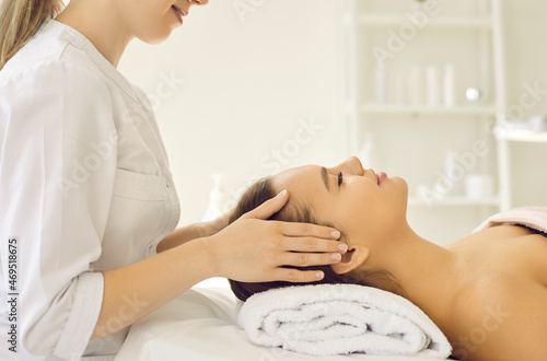 Happy young lady relaxing in spa salon or beauty parlour. Side view of beautiful woman lying on massage bed and getting cosmetic facial treatment for brighter complexion and better skin tone