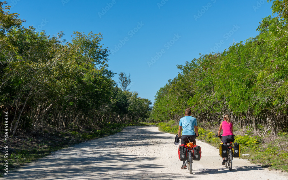 Two cyclists riding down a forested path in Cuba, enjoying a quiet moment surrounded by lush greenery Two cyclists riding down a forested path in Cuba, enjoying a quiet moment surrounded by lush greenery