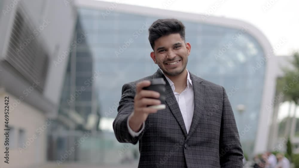 Portrait of handsome smiling Indian man in shirt and jacket, standing outdoors with coffee to go. Successful young Arab businessman, standing outside airport drinking coffee before business trip Portrait of handsome smiling Indian man in shirt and jacket, standing outdoors with coffee to go. Successful young Arab businessman, standing outside airport drinking coffee before business trip