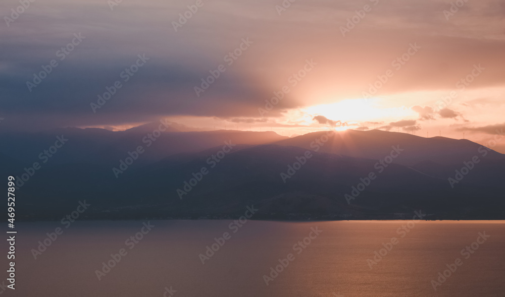 Fototapeta premium dramatic landscape with cinematic colors of sunrise rays light above mountains silhouette and sea, panoramic picturesque majestic view, fuzzy unfocused concept photo
