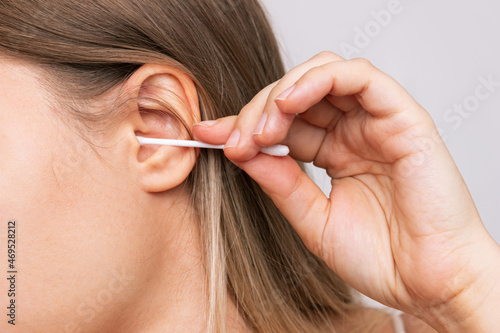 Cropped shot of a young caucasian woman cleaning her ear with a cotton swab isolated on a white background. Hygiene and health care. Close-up