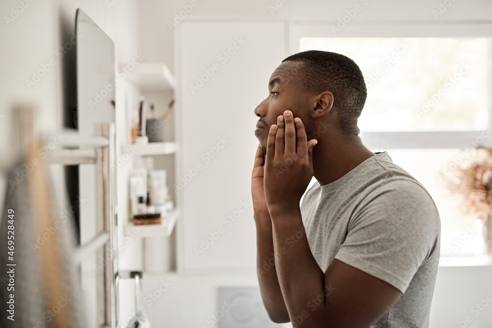 Young man African examining his complexion in his bathroom - obrazy, fototapety, plakaty 