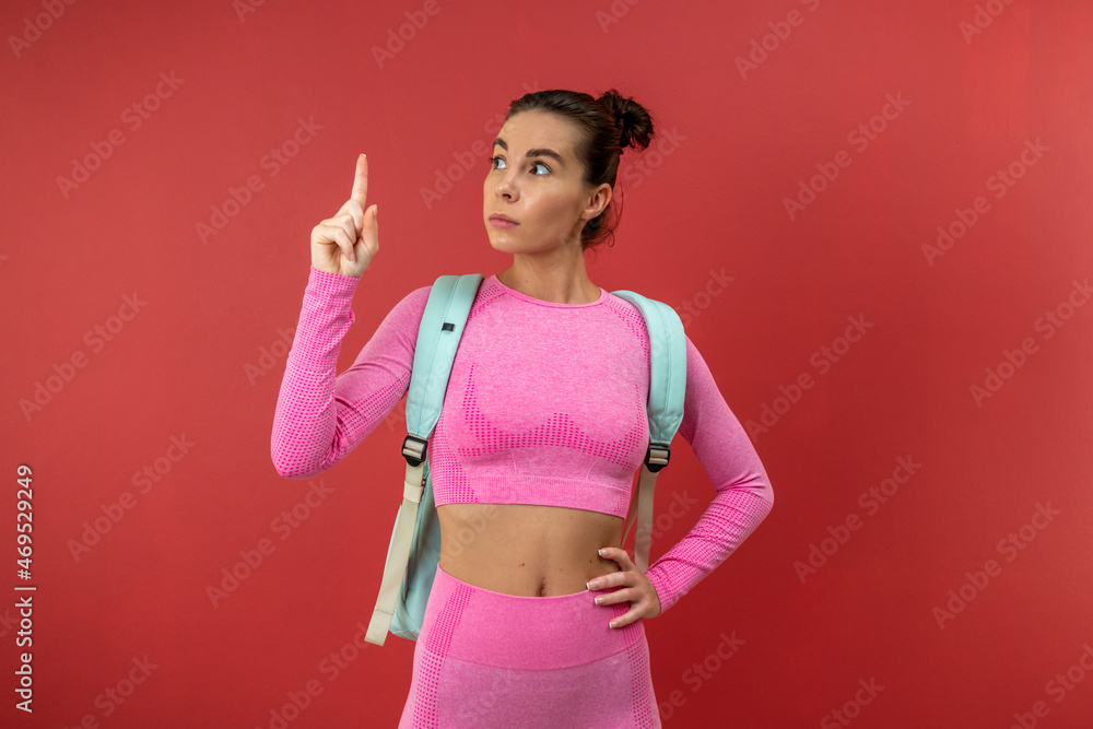 Young brunette wearing pink costume standing isolated on red background and pointing her finger up Young brunette wearing pink costume standing isolated on red background and pointing her finger up