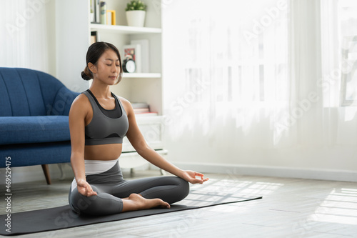 Calm of wellness Asian young woman sit on carpet breathing with yoga lotus pose,Yoga meditation of young healthy woman relax and comfortable at white cozy home,Yoga Exercise for Wellness Concept © 220 Selfmade studio