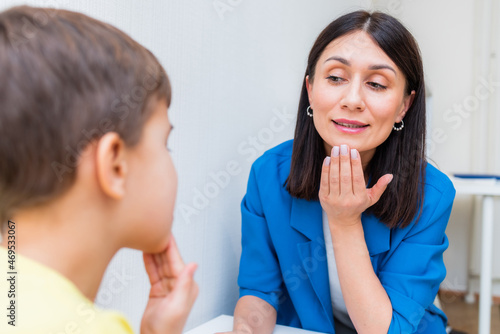 Woman speech therapist helps a boy correct the violation of his speech