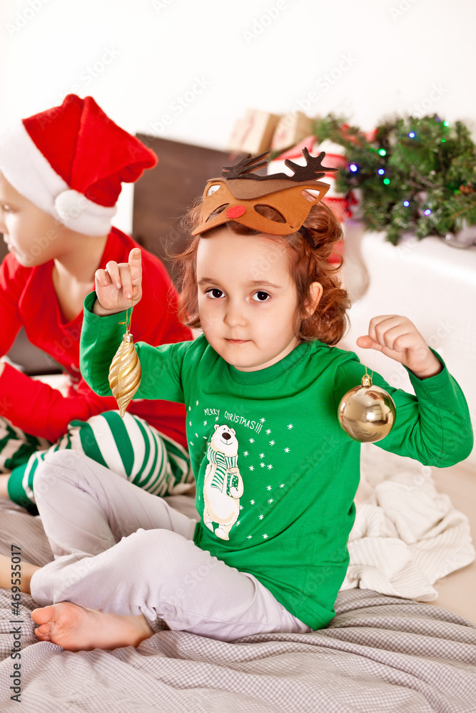 Little cute girl in funny deer mask and boy in Santa cap in Christmas pajamas get toys out of the box and get ready for the holiday. Little cute girl in funny deer mask and boy in Santa cap in Christmas pajamas get toys out of the box and get ready for the holiday.