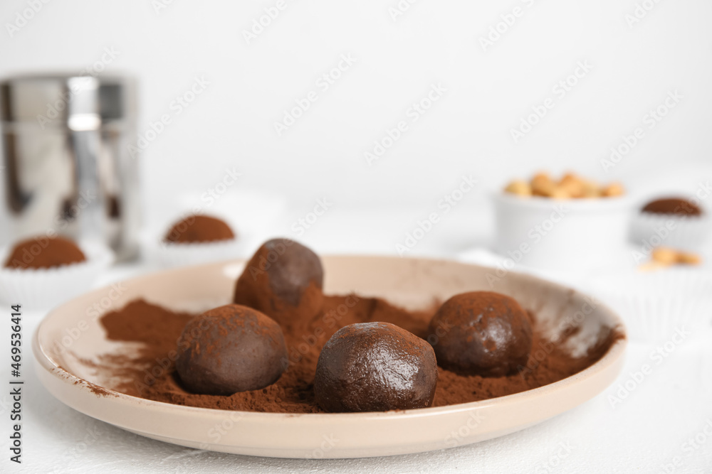 Plate with delicious chocolate truffles and cocoa powder on white table, closeup. Space for text Plate with delicious chocolate truffles and cocoa powder on white table, closeup. Space for text