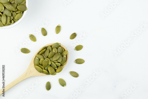 Peeled raw pumpkin seeds in a wooden spoon and and in small ceramic bowl on white background. Creative culinary concept. Culinary template for adding text.