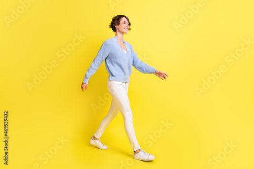 Photo of lovely girl walk look empty space wear blue cardigan trousers footwear isolated yellow color background