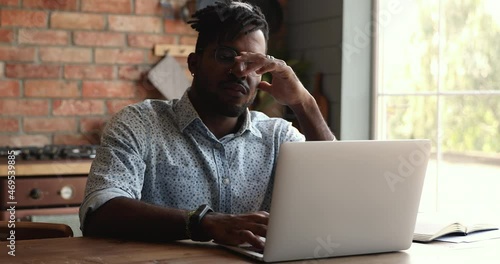 Concerned African man sit at table in kitchen use laptop read unpleasant news in e-mail, computer problem, financial breakdown, bankruptcy debt and crisis, downsizing at work, lost unsaved information photo