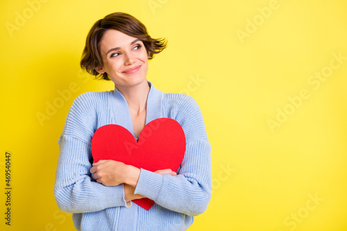 Photo of young attractive girl happy positive smile hug big heart dream dreamy look empty space isolated over yellow color background