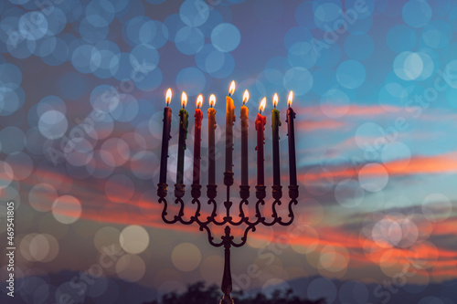 Burning festive candles are traditional symbols of Hanukkah Hebrew Holiday of Light, selective focus on menorah with burning  wax candles, blurred mountains, bokeh and dramatic dawn sky background 