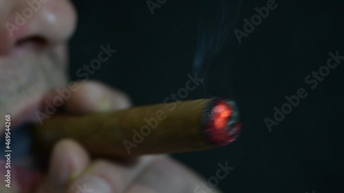 A man lights a cigar from a lighter on a dark background, close-up, selective focus. photo