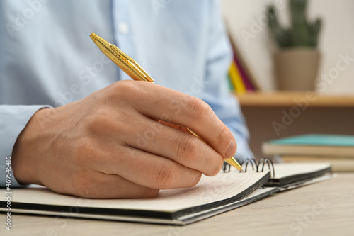 Man writing with pen in notebook at white wooden table, closeup of hand