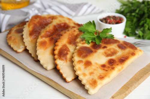 Board with delicious fried chebureki and parsley on white table