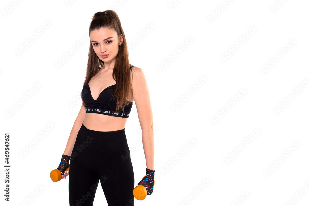Girl athlete stands with her hands down, holding yellow dumbbells, on a white background