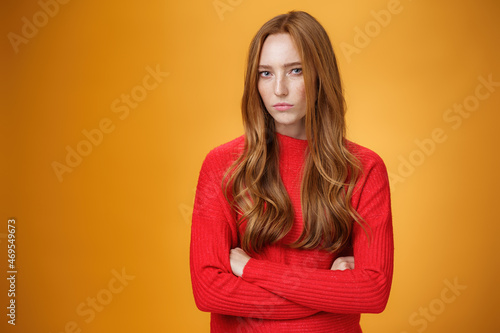 Suspicious intense and defensive ginger girl standing in passive-aggressive pose pouting and frowning looking with disbelief and disdain at camera, offended against orange background photo