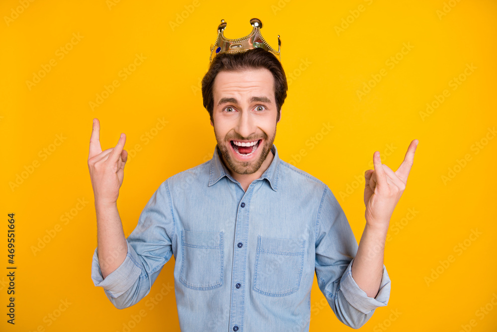 Photo of young excited man happy positive smile show rock sign crown king isolated over yellow color background Photo of young excited man happy positive smile show rock sign crown king isolated over yellow color background