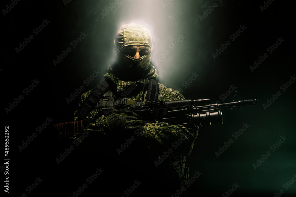Fototapeta premium A member of a special purpose unit. Russian special forces soldiers with submachine gun in clouds of smoke on a black background with colored illumination.