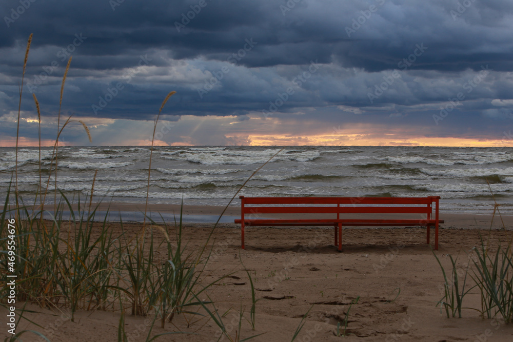 Lonely red bench on the beach by the sea at sunset Lonely red bench on the beach by the sea at sunset