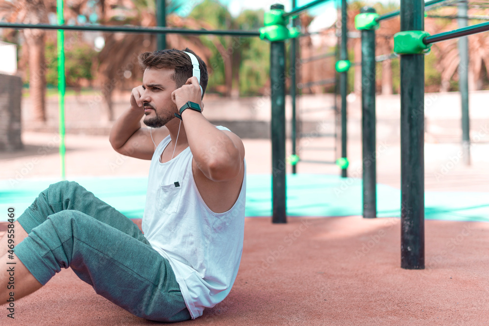 Young sportsman is training on the sports ground outdoor and listening to music. Healty lifestyle