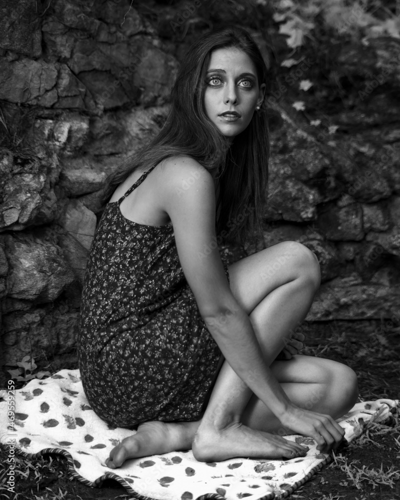 Naklejka premium Black and white image of a young woman in flower print dress, exploring a woodland garden.