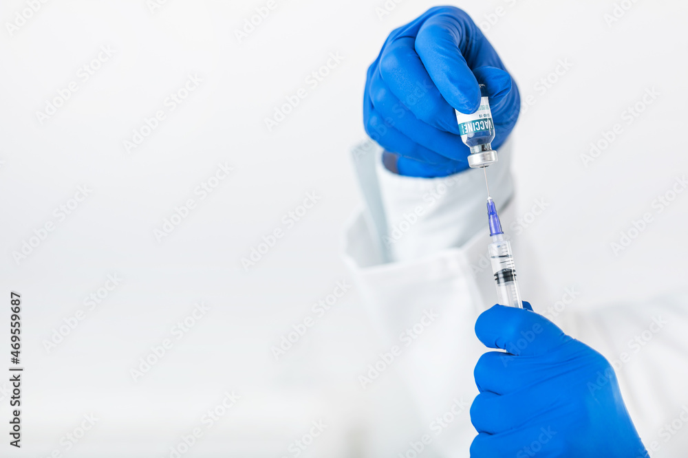 Close up of doctor hands in blue rubber gloves holding vaccine bottle and syringe. Medical worker preparing drugs for patient. Health treatment concept.