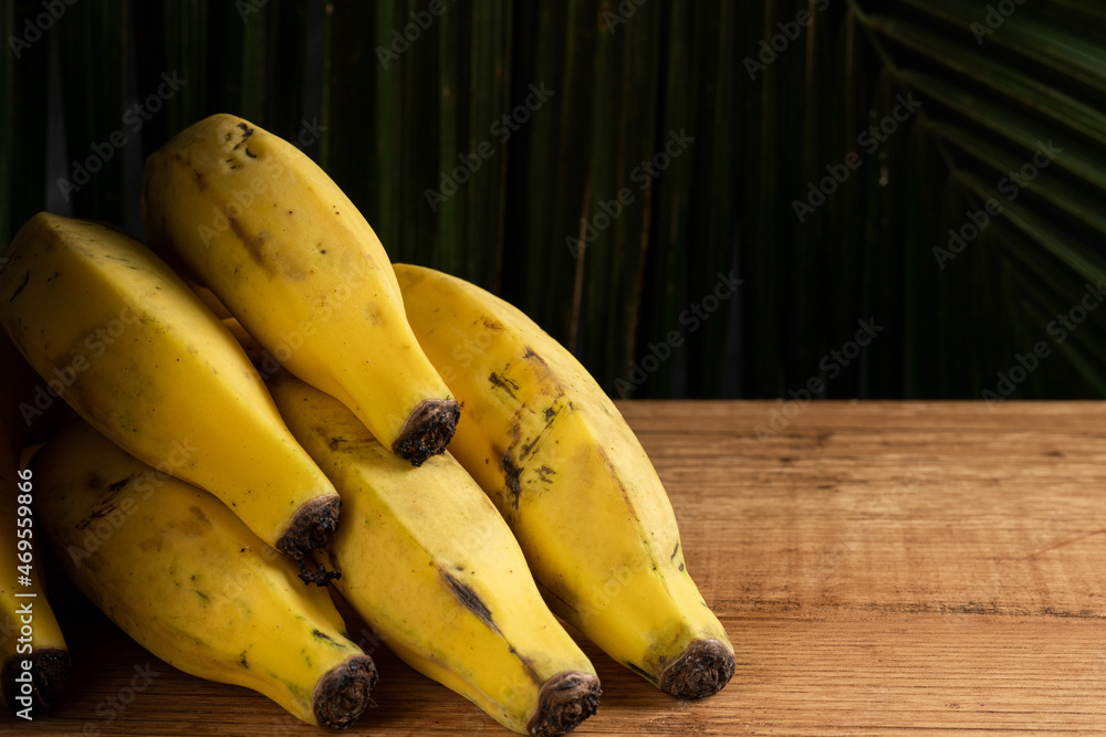 Bananas on wooden desk with palm tree leafs on dark background. Bananas on wooden desk with palm tree leafs on dark background.