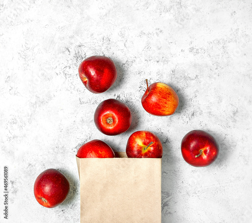 Red apples in a paper bag on a white marble background.