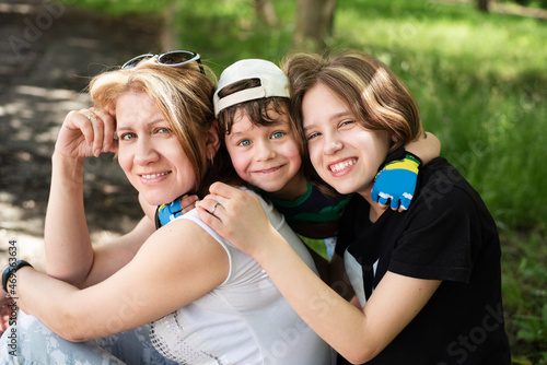 The little boy happily hugs his favorite girls - mom and sister, they rest together in the park after a walk and games in the fresh air. Mom with children together