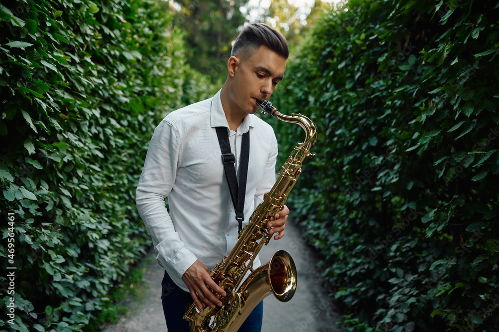 Fototapeta premium Male saxophonist plays on the alley in summer park