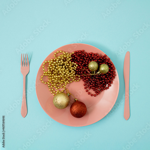 Creative flat lay with pink plate with cutlery, spoon kinfe and fork , abstract Christmas decoration on colored background pink and light blue. with baubles and christmas three balls. photo