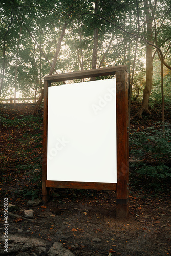 Wooden-framed old poster in the woods. Mock-up of forest guidepost. Environment friendly advertisement banner.