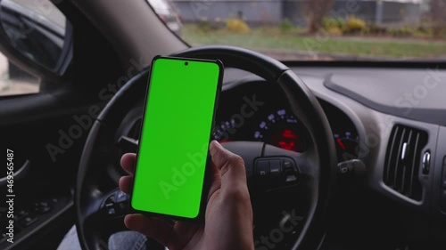 Using the phone while driving in the car. Phone with a green screen for your inscription. Copy space on your phone