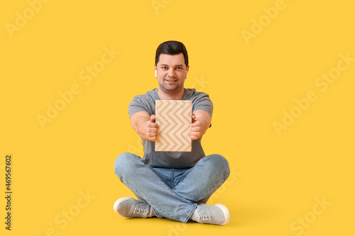 Young man with book and earphones on color background © Pixel-Shot