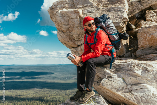 A male tourist is resting after a hard climb up the mountain. A traveler among the Rocky Mountains. A man is a traveler with a backpack among the rocks. Backpacking in the mountains. Copy space