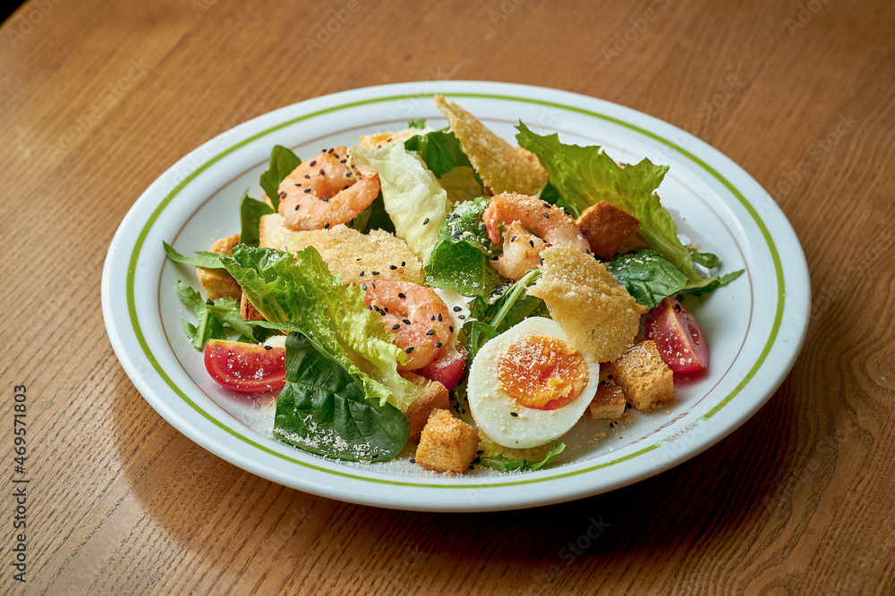 Caesar salad with shrimp and parmesan in a white plate on a wooden background Caesar salad with shrimp and parmesan in a white plate on a wooden background