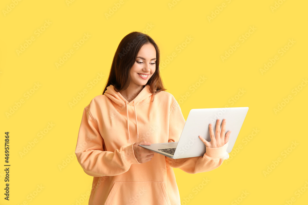 Beautiful young woman in stylish hoodie and with laptop on color background Beautiful young woman in stylish hoodie and with laptop on color background