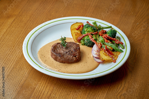 Beef steak with black pepper sauce and vegetables steamed on a white plate on a wooden background
