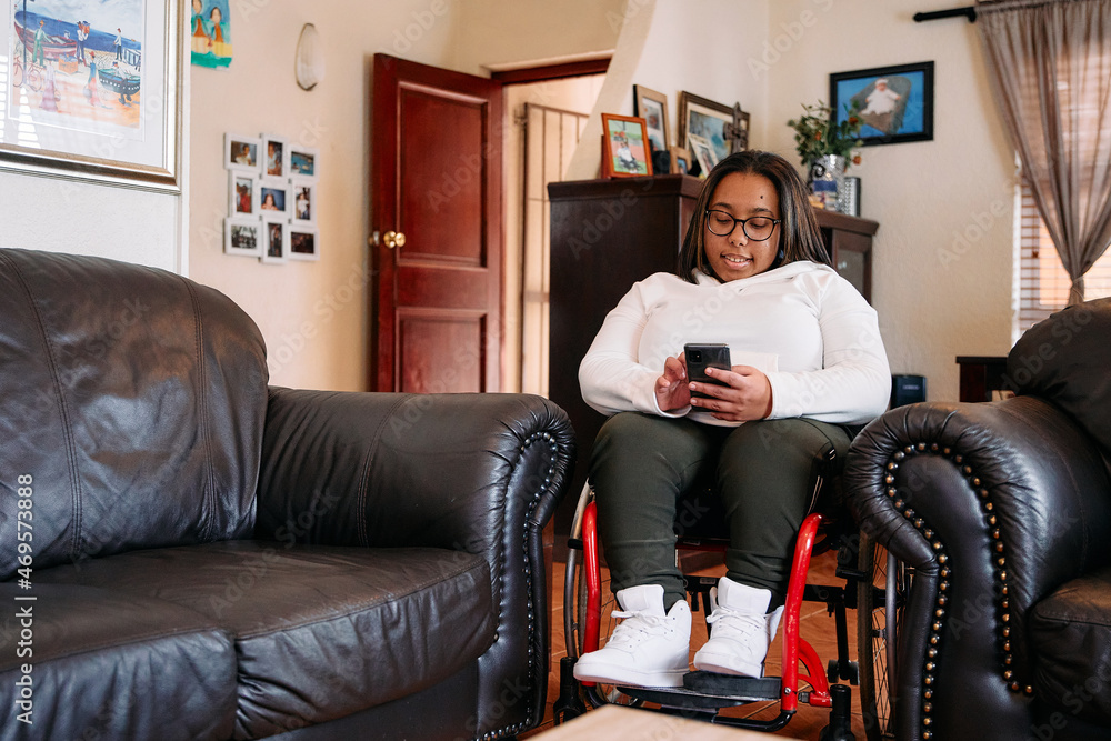© PICHA - Young woman in a wheelchair checking her phone at home © PICHA - Young woman in a wheelchair checking her phone at home