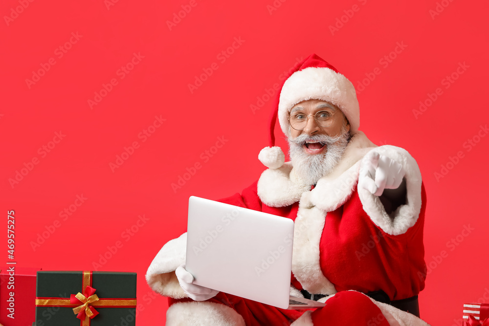 Santa Claus with laptop pointing at viewer on color background Santa Claus with laptop pointing at viewer on color background