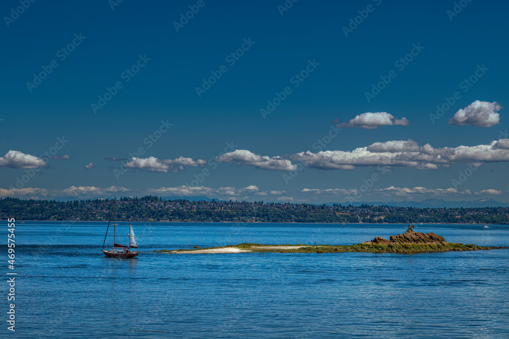 2021-11-16 A SAIL BOAT AND A SMALL ISLAND IN THE PUGET SOUND OFF OF BAINBRIDGE ISLAND WASHINGTON WITH THE MAGNOLIA NEIGHBORHOOD IN THE BACKGROUND 