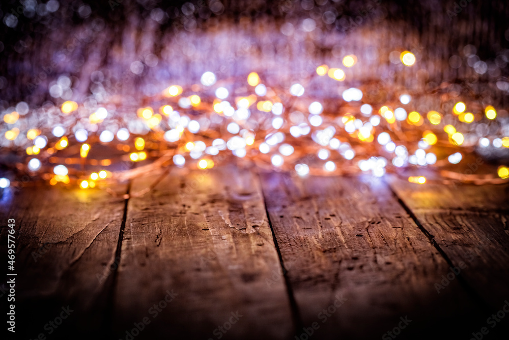 christmas garland of white and golden defocused lights on dark old weathered vintage table or wooden brown board. Christmas decoration, New Years Eve. Selective focus, bokeh, space for text.