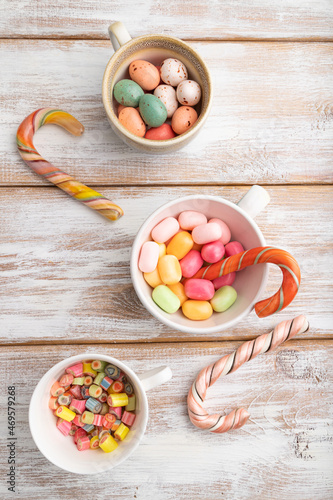 Heap of multicolored caramel candies in cups on white wooden background. top view.