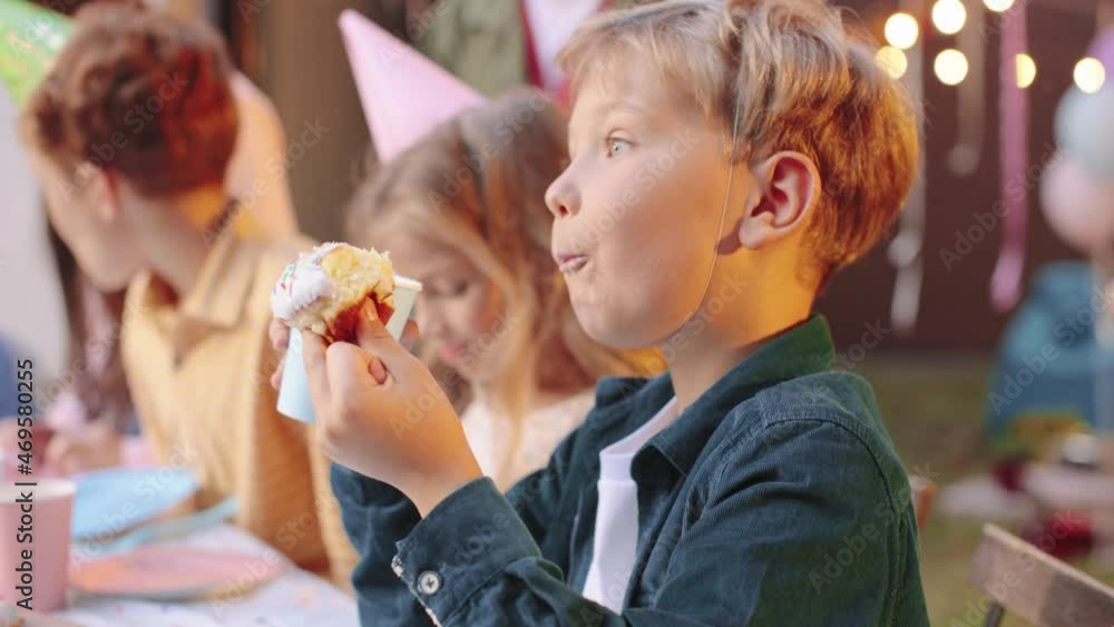 Group of multiracial children eating cake while having outdoor birthday party together. Holidays concept